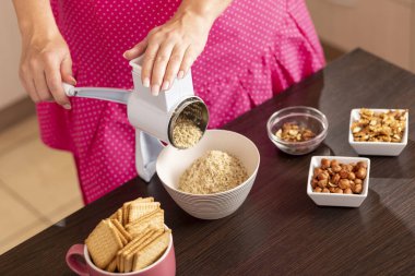 Önlük takmış, ceviz öğütücüyle mutfakta ceviz öğüten bir kadının yüksek açılı görüntüsü. Öğütme makinesinin tepesini tutan ele odaklan.