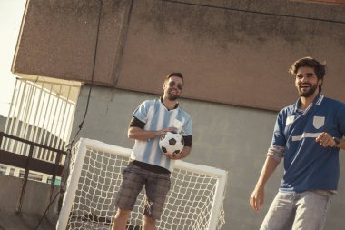 Genç arkadaşlar binanın terasında futbol oynarken eğleniyorlar, maçtan önce ısınıyorlar.