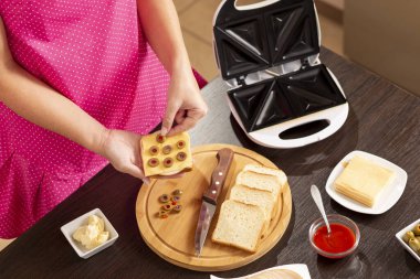 Bir sandviçe zeytin ekleyen kadın elleri; sandviç makinesinde kahvaltıda sıcak sandviç hazırlayan kadın.