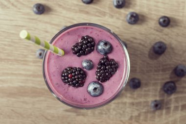 Masaya bir avuç yabanmersini konmuş bir sehpanın üzerine yerleştirilmiş bir bardak yaban mersinli smoothie 'nin üst görüntüsü