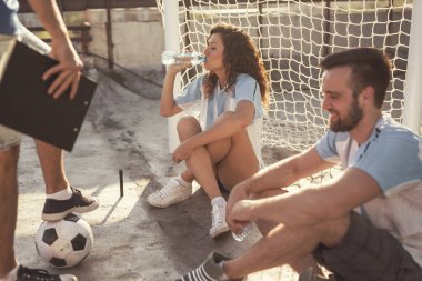 Bir grup genç arkadaş, çatı terasında futbol oynarken mola veriyor, kalenin yanında oturuyor, su içiyor ve dinleniyor.