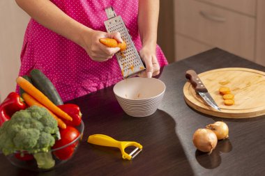 Kadın ellerinin mutfak tezgahında taze sebze salatası yapmak için rendelenmiş taze havuç rendelemesi.