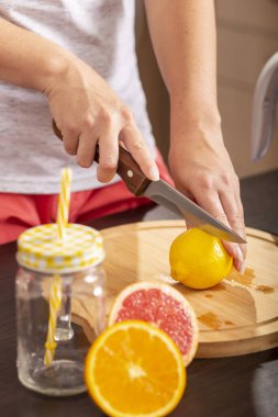 Bir mutfak bıçağı tutan ve bir kesme tahtasına limon kesen kadın elleri; mutfak tezgahında taze sıkılmış turunçgil meyvesi yapan kadın