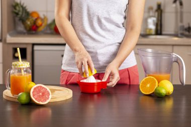 Limonun yarısını tutan ve limon sıkacağı ile sıkan kadın elleri; mutfak tezgahında limonata yapan kadın.