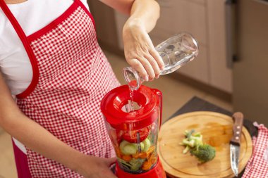 Sebze suyu yapmak için taze sebze kabının üzerine kadın ellerinin suyu döktüğü yüksek açılı bir manzara. Suya odaklan.