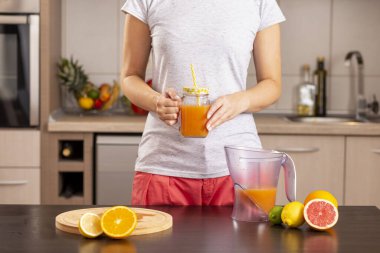 Mutfak tezgahında hazırladıktan sonra taze sıkılmış narenciye suyuyla dolu bir kavanozu tutan kadın elleri.