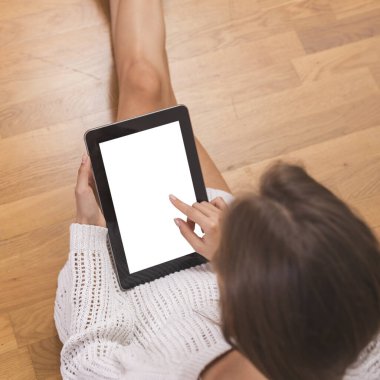 Ahşap zeminde oturan, süveter giyen ve tablet bilgisayar kullanan güzel bir kadının ayrıntıları.