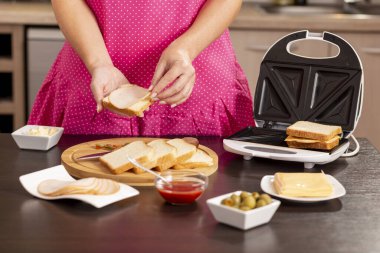 Bir sandviçe salam ekleyen kadın elleri, sandviç makinesinde kahvaltıda sıcak sandviç yapan kadın. Ellere ve sandviçe odaklan.