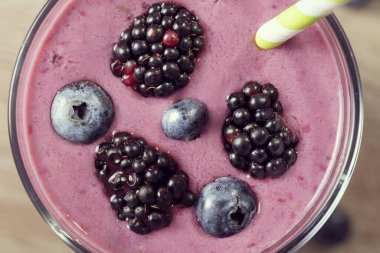 Bir bardakta yaban mersini, böğürtlen ve muzlu smoothie 'nin ayrıntıları. Yüzeyinde saman ve meyve süslemesi var.