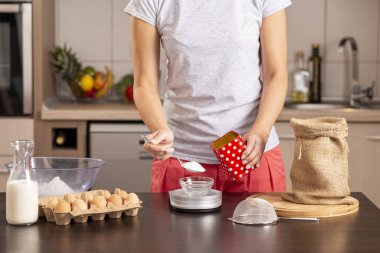 Şekeri ölçmek için mutfak terazisi kullanan kadın ellerinin ayrıntıları; pasta yapmak için malzeme ölçen kadın. Kaşık ve ele odaklan.