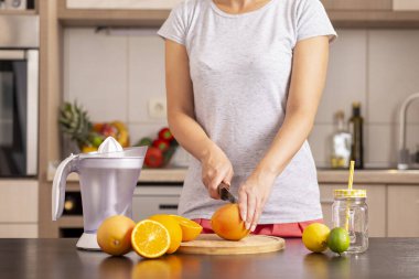 Bir mutfak bıçağı tutan ve bir kesme tahtasına limon kesen kadın elleri; mutfak tezgahında taze sıkılmış turunçgil meyvesi yapan kadın
