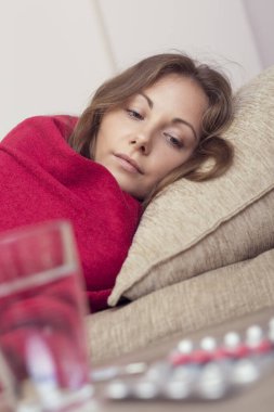 Yatağında battaniyeyle yatan hasta kadın yüksek ateş ve grip. İlaçlar ve bir bardak su masanın üstünde.