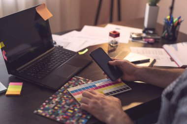 Tasarımcının ellerinin çizim tahtası kullanarak renk paletinden bir renk seçmesinin ayrıntıları. Başparmağına ve telefona odaklan.