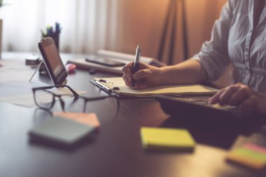 Hesap makinesi kullanan ve hesaplamaları çizelgeye yazan kadın ellerinin ayrıntıları. Ev ofisinde çalışan iş kadını. Kalemin ucuna odaklan.