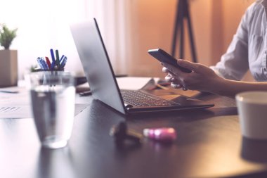 Akıllı bir telefon tutan kadın elleri, ofiste oturan iş kadını, akıllı bir telefona mesaj yazan. Seçici odak