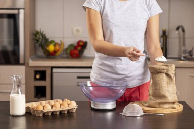 Un ölçmek için mutfak terazisi kullanan kadın ellerinin ayrıntıları; kek yapmak için malzeme ölçen, çuval bezinden un alan kadın