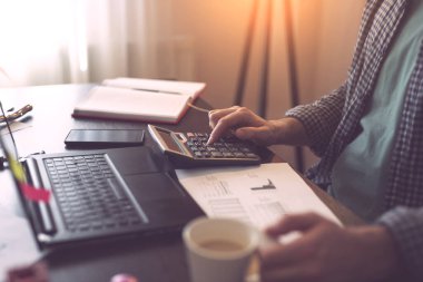 Hesaplama yapmak için hesap makinesi kullanan bir erkek işadamının ellerinin ayrıntıları, ev ofisinde fazla mesai yapmak. İşaret parmağına odaklan.