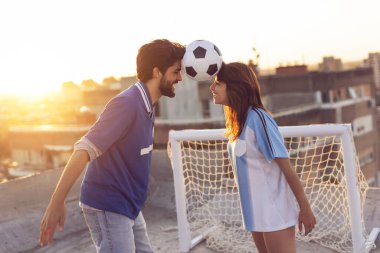 Genç çift, futbol oynadıktan sonra çatıda eğleniyor, dans ediyor ve kafalarının arasındaki topla dengede duruyor.