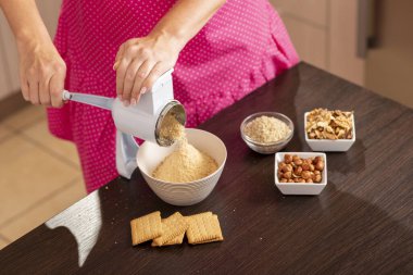 Bisküvi öğütme makinesinde bisküvi öğüten bir kadının yüksek açılı görüntüsü. Öğütme makinesinin tepesini tutan ele odaklan.