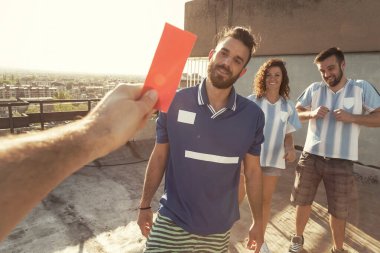 Futbol oynayan bir grup insan, hakem faulden sonra oyunculardan birine kırmızı kart veriyor; insanlar kızgın ve futbol oynarken kavga ediyorlar