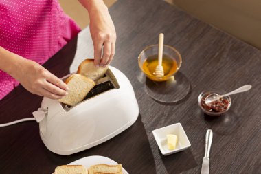 Kadın ellerinin tost makinesine ekmek dilimleri koyup kahvaltıda kızarmış ekmek yaptığı yüksek açılı manzara. Eline ve ekmek dilimine odaklan.