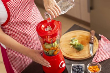 Sebze suyu yapmak için taze sebze kabının üzerine kadın ellerinin suyu döktüğü yüksek açılı bir manzara. Şişenin ucuna ve eline odaklan.