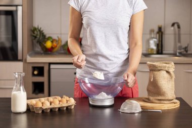 Un ölçmek için mutfak terazisi kullanan kadın ellerinin ayrıntıları; kek yapmak için malzeme ölçen, çuval bezinden kaşıkla un alan kadın