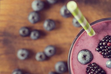 Kırsal kesim tahtasına yerleştirilmiş bir bardaktaki yabanmersinli smoothie 'nin en üst görüntüsü.