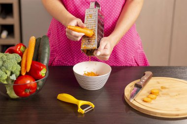 Kadın ellerinin mutfak tezgahında taze sebze salatası yapmak için rendelenmiş taze havuç rendelemesi.