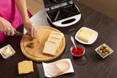 Kadın ellerinin kesme tahtasındaki sandviçler için zeytin keserken yüksek açılı görüntüsü kahvaltıda sandviç makinesinde sıcak sandviç yapan kadın.