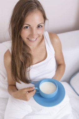 Güzel, genç bir kadın akşamları yatağında oturuyor, elinde ılık sütle dolu büyük mavi bir bardak tutuyor, iyi geceler için içiyor.