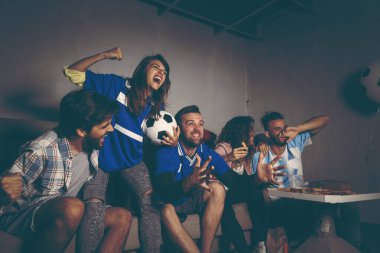 Bir grup genç arkadaş, bir binanın çatısında futbol maçı izleyip takımlarının gol atmasını kutluyorlar.