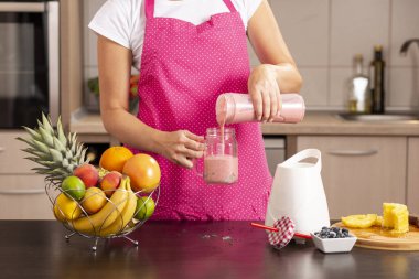Bir kavanoza yeni yapılmış ahududu smoothie dolduran kadın elleri; mutfakta önlük giymiş bir kadın, kahvaltıda smoothie hazırlıyor.