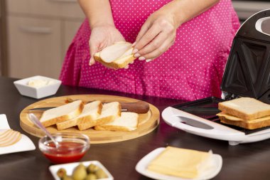 Bir sandviçe salam ekleyen kadın elleri; sandviç makinesinde kahvaltıda sıcak sandviç yapan kadın.