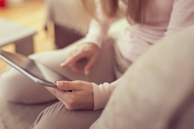 Oturma odasındaki kanepede oturan, elinde tablet bilgisayarla internette sörf yapan güzel bir genç kızın ayrıntıları.