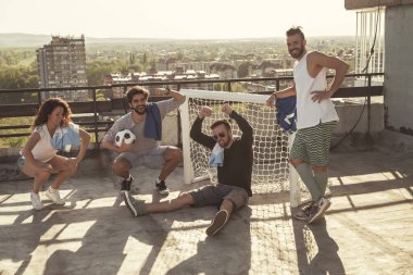 Bir grup genç arkadaş terasta futbol oynadıktan sonra rahatlıyor, birlikte dışarıda vakit geçiriyorlar.