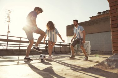 Güneşli bir yaz gününde çatıdaki terasta forma giyen gençler futbol oynarken eğleniyorlar.