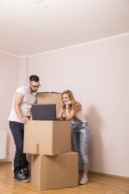 Aşık genç bir çift yeni bir daireye taşınıyor, karton kutuların yanında duruyor, dizüstü bilgisayara bakıyor ve yeni evlerini yeniden dekore etmeyi planlarken internette geziniyorlar.