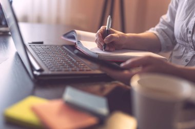 İş kadınının elinde cep telefonu olan ve bir ajandaya yazı yazan ellerinin ayrıntıları. Kalemin ucuna ve parmaklarına odaklan.