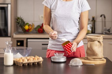 Şekeri ölçmek için mutfak terazisi kullanan kadın ellerinin ayrıntıları; pasta yapmak için malzeme ölçen kadın. 