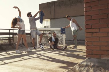 Bir grup genç arkadaş terasta futbol oynamadan önce esniyor ve ısınıyor. Birlikte dışarıda vakit geçiriyorlar.