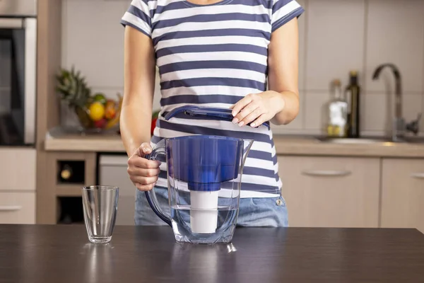 Detail of female hands holding a filtered water pitcher and putting a cap on it after filling it with a tap water to be filtered