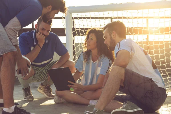 Group of young friends playing a football match on a building rooftop, on a time out, discussing the game strategy. Focus on the girl