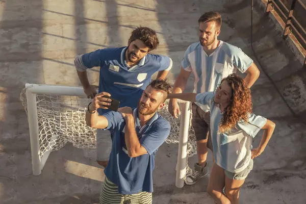 High angle view of group of football fans having fun taking a selfie on a building rooftop terrace before the game; friends taking selfies while playing football