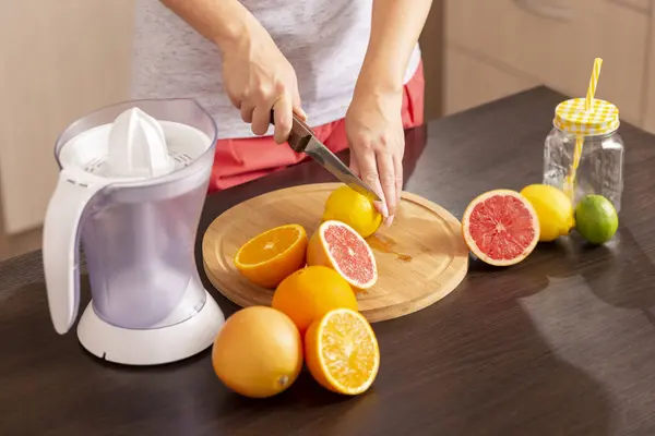 Bir mutfak bıçağı tutan ve bir kesme tahtasına limon kesen kadın elleri; mutfak tezgahında taze sıkılmış turunçgil meyvesi yapan kadın