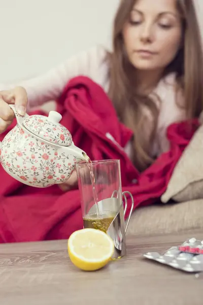 病気の女性は 高熱とインフルエンザでベッドに横たわり ガラスにティーポットからお茶を注いでいます テーブルの上のレモンと丸薬 ティーポットに焦点を当てる — ストック写真