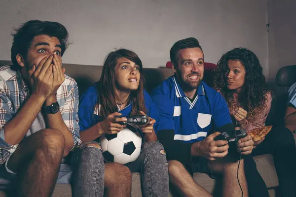 Group of young friends having fun on a buidling rooftop terrace while playing a football video game