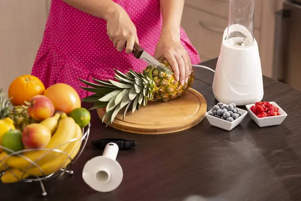 Ananas kesiciyle soymak için mutfak bıçağıyla ananas kesen bir kadının yüksek açılı görüntüsü.