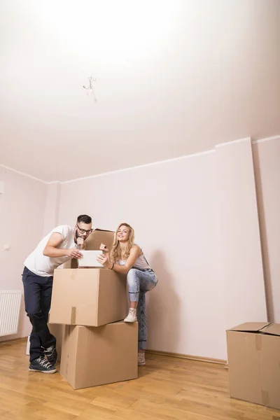 若いカップルは 新しいアパートに移動するのが大好きで 段ボール箱の隣に立って タブレットコンピュータを保持し 新しい家を改装することを計画している間 ウェブサーフィン — ストック写真