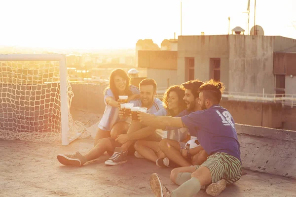Grupa Młodych Ludzi Siedzących Dachu Budynku Koszulkach Odpoczywających Meczu Piłki — Zdjęcie stockowe